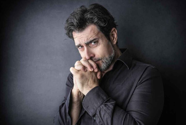 Thoughtful man with clasped hands, seeking depression therapy and emotional support.